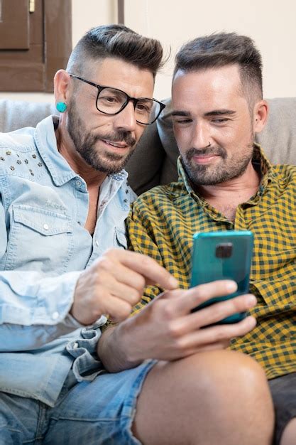 Feliz jovem casal gay usando telefone celular enquanto está sentado em um sofá na sala de estar