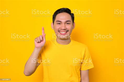 Excited Young Asian Man In Casual Tshirt Pointing Finger Up Having An