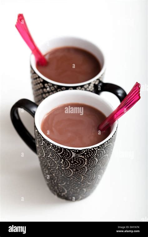 Closeup Of Two Mugs Of Hot Chocolate With Red Plastic Spoons On Light