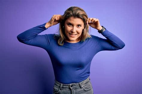 Junge schöne blonde Frau trägt lässiges T Shirt vor isoliertem violettem Hintergrund und zieht