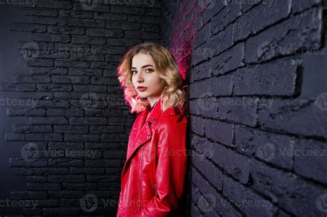 Studio Portrait Of Blonde Girl In Red Leather Jacket Against Brick Wall Stock Photo At