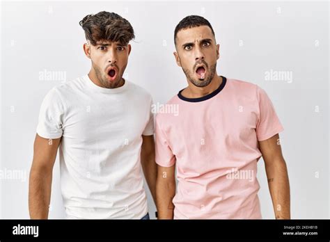 Jeune couple gay debout sur fond isolé dans le visage de choc regardant sceptique et
