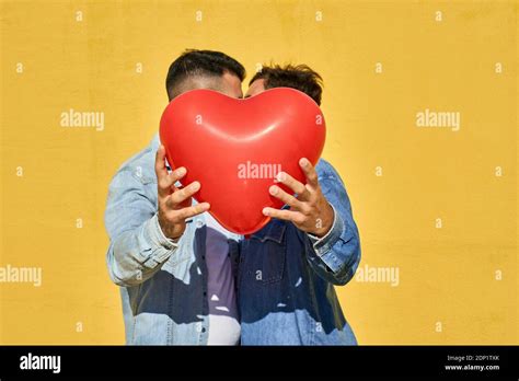 Gay Men Holding Balloon While Kissing Against Yellow Wall Stock Photo Alamy