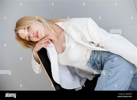 Blonde Woman In White Jacket And Jeans Sitting On Chair At Home Stock Photo Alamy