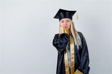 Fille blonde en robe de graduation et casquette envoyant des baisers et mettant la main près de