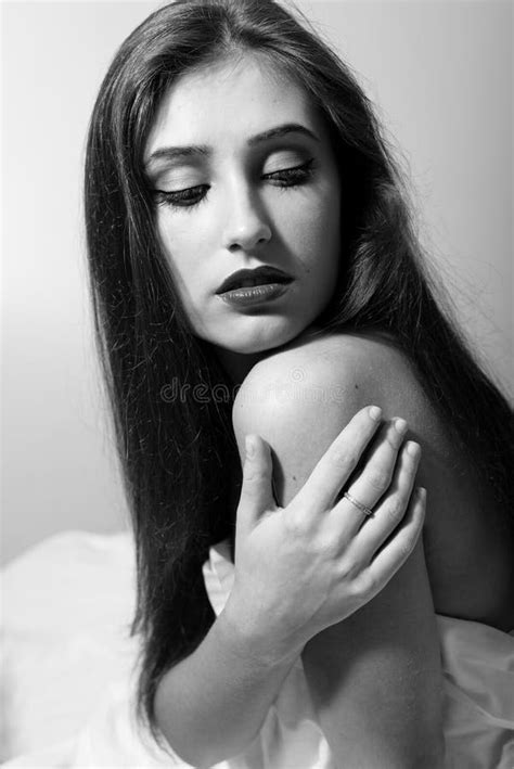Portrait Of Seductive Woman Touching Her Naked Shoulder Looking Down Sitting On White Bed Black