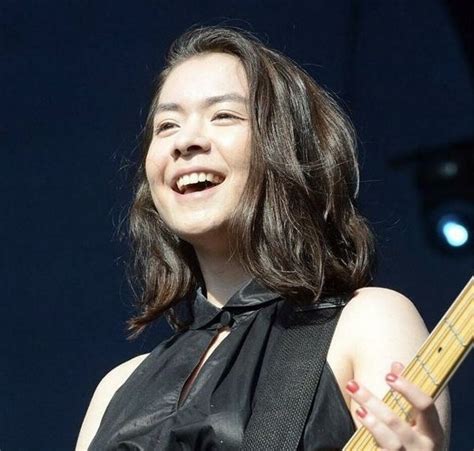 A Woman Holding A Guitar And Smiling At The Camera While Standing In