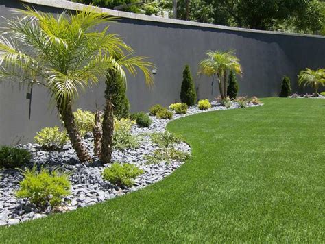 A Garden With Palm Trees And Rocks In Front Of A Gray Wall That Says