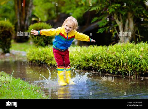 Child Playing In Puddle Kids Play And Jump Outdoor By Autumn Rain