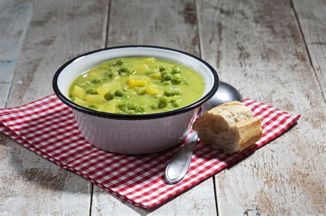 Enamel Bowl Of Pea Stew Spoon And Sliced Baguette On Cloth And Wood