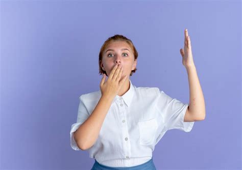 Jeune fille russe blonde surprise met la main sur la bouche avec la main levée isolé sur fond