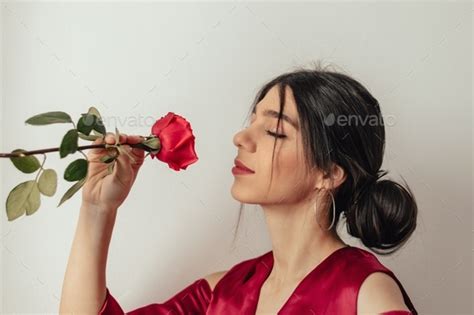 Beautiful Latina Brunette Girl In Red Dress Sniffs Rose Stock Photo By Buzmakovatatyana