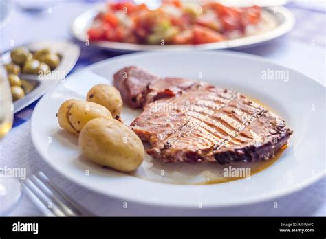 Tuna Steak Accompanied With Potatoes Olives Tomato Salad And Wine On