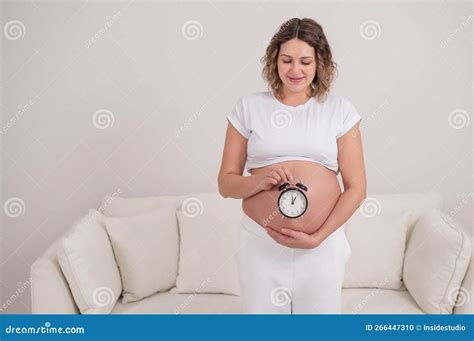 A Pregnant Woman With A Naked Belly Holds An Alarm Clock Intended Date Of Birth Stock Photo