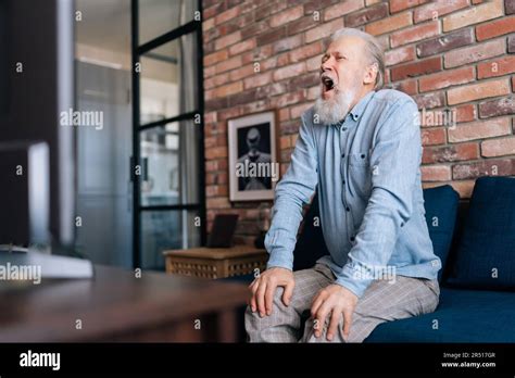 Happy Excited Grey Haired Mature Football Fan Sitting At TV Screen And Cheering For Favorite