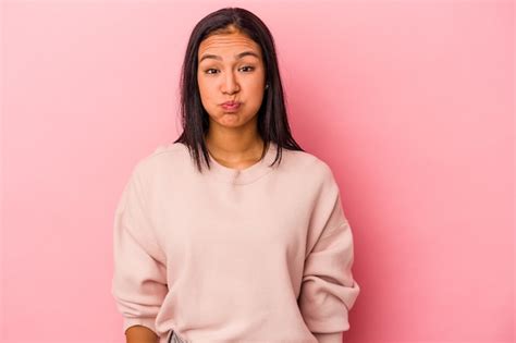 Joven latina aislada sobre fondo rosa sopla mejillas tiene expresión cansada concepto de