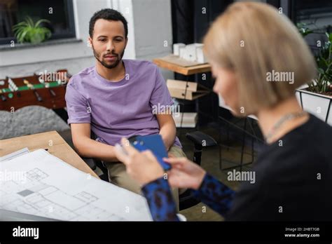 African American Interior Designer Looking At Blurred Blonde Colleague With Sample Stock Photo