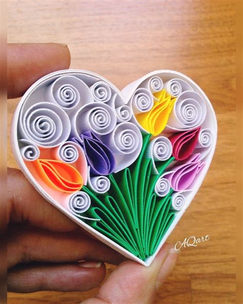 A Hand Holding A Heart Shaped Origami Decoration With Flowers In The