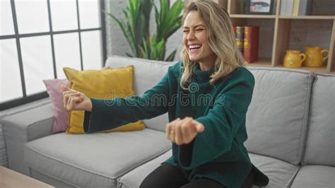 A Joyful Blonde Woman In A Cozy Living Room Laughing And Gesturing Playfully Stock Photo Image