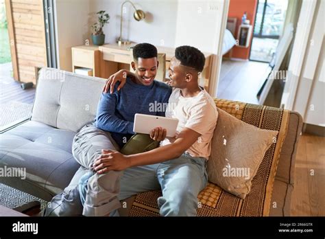 Un jeune garçon gay heureux qui se serre et utilise une tablette numérique sur le canapé Photo