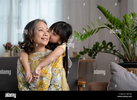 Granddaughter Kissing With Love Her Mature Woman Grandmother Preschooler At Home On Sofa Stock