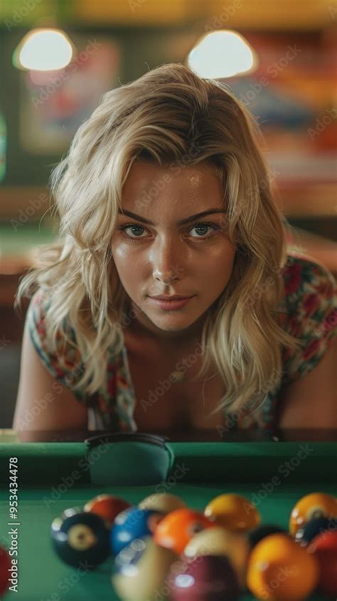 A Serious Blonde Woman In A Floral Shirt Leans On A Pool Table With Billiard Balls In A Rack