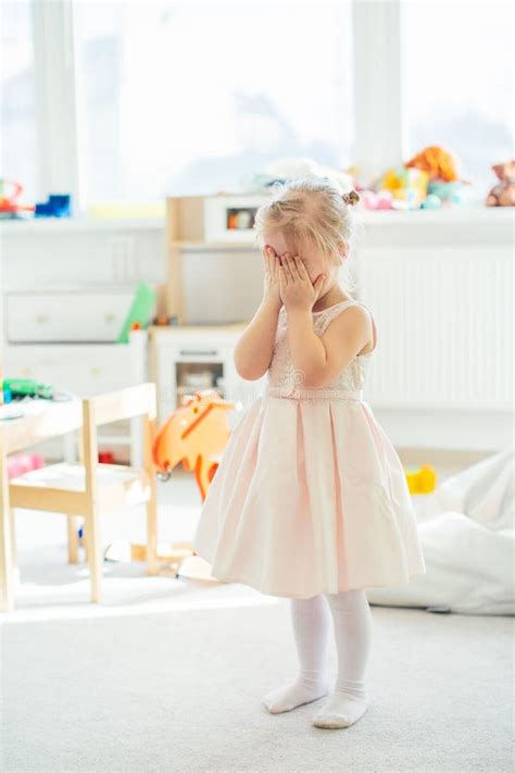 Adorable Petite Fille Blonde En Robe Rose Qui Se Cache Le Visage Derrière Les Mains Image stock