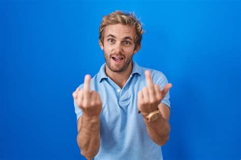 Free Photo Caucasian Man Standing Over Blue Background Showing Middle Finger Doing Fuck You