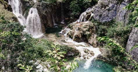 Picturesque Waterfalls Flowing Through Rocky Ravine In Green Lush