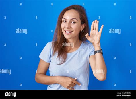 Brunette Woman Standing Over Blue Background Waiving Saying Hello Happy And Smiling Friendly