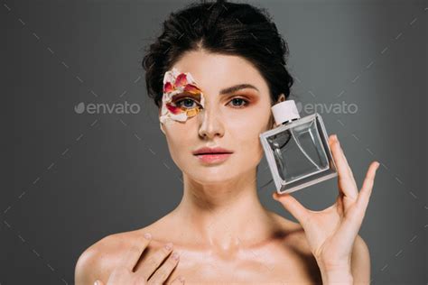 Portrait Of Naked Girl With Petals On Face Holding Perfume Bottle Isolated On Grey Stock Photo