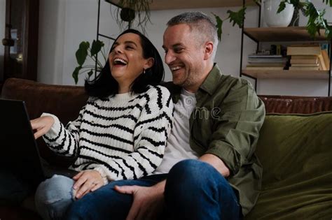 Happy Couple Laughing While Looking At Videos On Laptop Sitting On