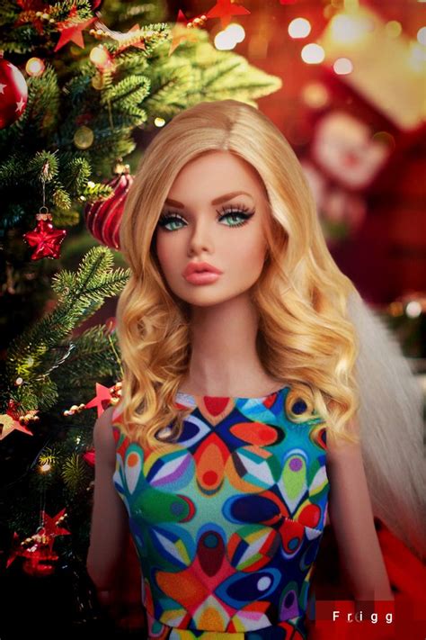 A Blonde Doll Wearing A Colorful Dress Next To A Christmas Tree With Lights On It