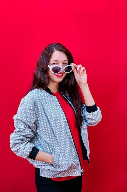 Premium Photo Portrait Of A Smiling Young Brunette Girl Taking Off Her Sunglasses On Flat Red