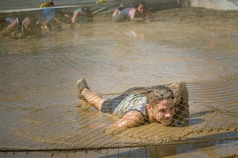 Competitor Crawling Through Mud In Obstacle Course Editorial Stock