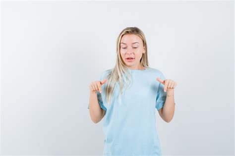 Fille blonde pointant vers le bas avec l index en t shirt bleu et à la jolie vue de face