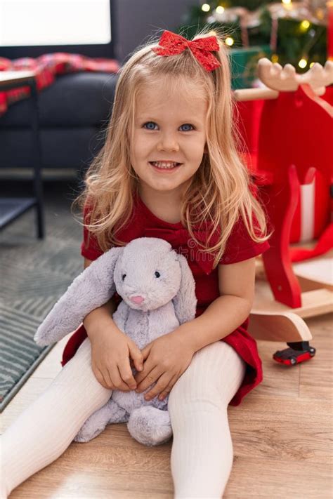 Adorable Blonde Girl Smiling Confident Sitting On Floor By Christmas Tree At Home Stock Image