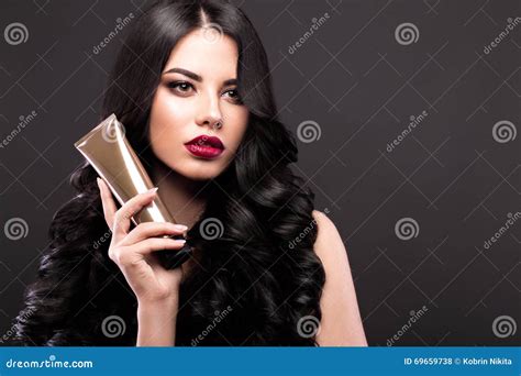 Beautiful Brunette Model Curls Classic Makeup And Red Lips With A Bottle Of Hair Products The
