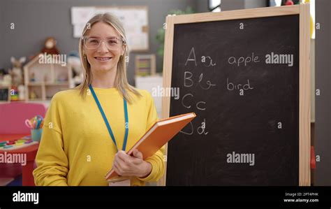 Jeune femme blonde enseignante maternelle écrivant un exercice de vocabulaire sur le tableau