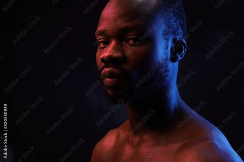 Portrait Of A Handsome Black Man In Red And Blue Light On Dark Background With Naked Sports