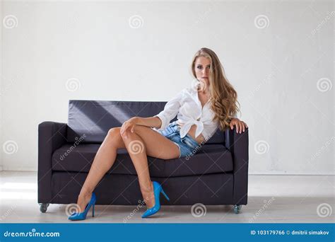 Beautiful Blonde Girl With Blue Eyes Sitting On The Couch In A White Room 1 Stock Photo Image