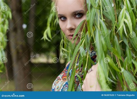 El Blonde Blando Dulce Hermoso De La Muchacha Con Los Ojos Azules Se Coloca Cerca De Un árbol