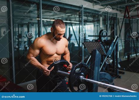 A Hot Handsome Man In Black Shorts With Naked Muscular Torso Holds A Barbell On A Blurred Blue