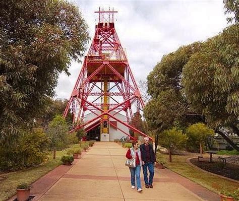 two people walking down a path in front of a red tower with a clock on it