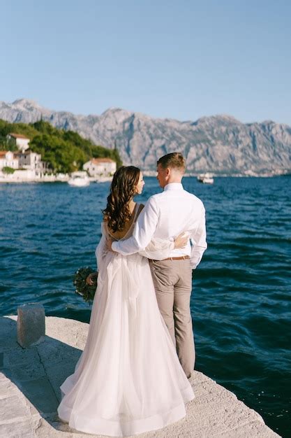 Premium Photo Bride And Groom Stand Hugging On The Pier And Look At