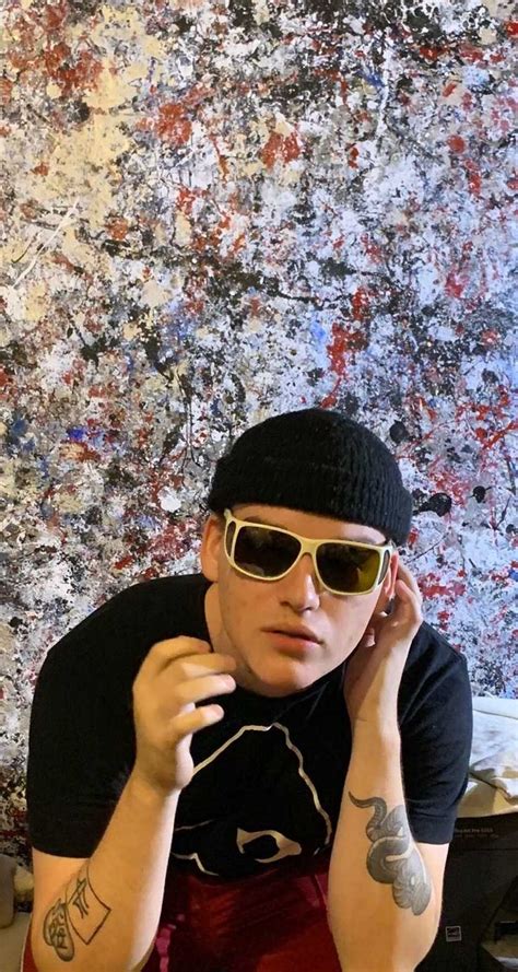 a man wearing sunglasses and a beanie sitting in front of a wall