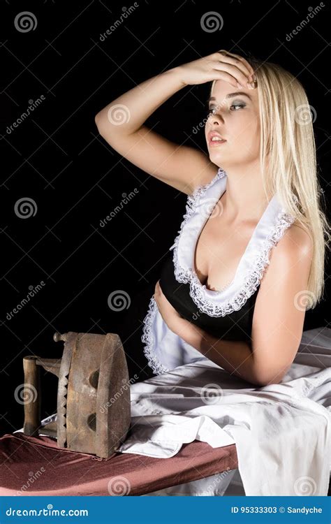 Blonde Woman In Housekeeper Suit Ironing White Shirt With Old Iron Retro Style On A Dark