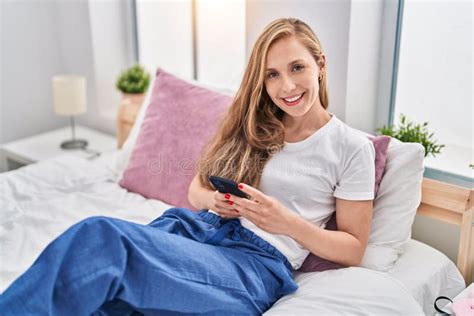 Jeune Femme Blonde Utilisant Son Smartphone Au Lit Souriant Avec Un Sourire Heureux Et Cool Au