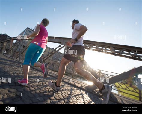 Healthy Mature Couple Jogging In The City At Early Morning With Sunrise In Background Stock