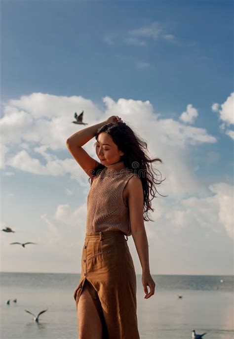 Happy Asian Woman With Hands In The Air Walks On The Seaside In Autumn